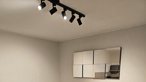 Uma sala de estar moderna com um sofá, um pequeno armário de madeira, uma mesa de centro de vidro e um lustre.