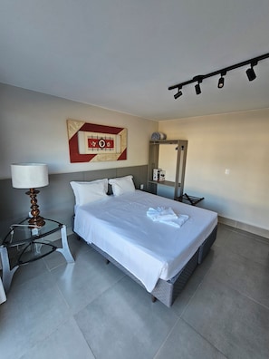 Et hotelværelse med en seng, et natbord med lampe, et spejl og et vægur.