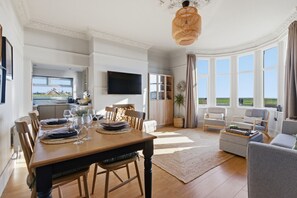 Ein geräumiger Wohnbereich mit Esstisch, einer Couch und einem an der Wand befestigten Fernseher.