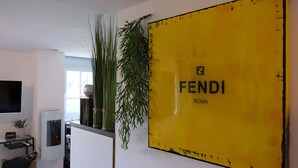 A room with a yellow wall, a television mounted on the wall, a plant, and a window. - Holiday Apartment for 2 People (40 m²) in Kerpen (Eifel) (Kerpen (Eifel))