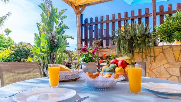A table set with plates, a glass of orange juice, a bowl of pastries, and a fruit basket. - Cubo's Marala Rural House / Private pool / BBQ / Terrace / Free Wi-Fi (Alhaurín el Grande)