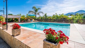 A swimming pool with a stone border, surrounded by potted plants and a wooden fence. - Cubo's Marala Rural House / Private pool / BBQ / Terrace / Free Wi-Fi (Alhaurín el Grande)