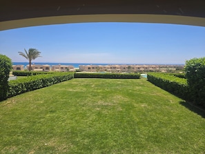 Ein gepflegter Rasen, ein Schwimmbecken und Blick auf eine Küstenlandschaft mit Gebäuden.