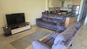 A living room with a TV, sofa, and kitchen in the background.