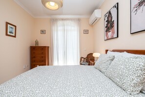 Ein Schlafzimmer mit einem Bett, einem Schminktisch, einem Sessel, einer Lampe und einem Fenster mit Vorhängen.