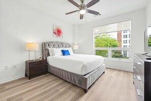 Ein Schlafzimmer mit Bett, Nachttisch, Lampe, Deckenventilator, Fenster und Kommode.