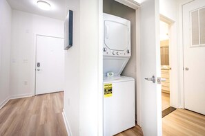 Ein Waschraum mit Waschmaschine und Trockner, einer Tür mit Griff und einem Lichtschalter an der Wand.