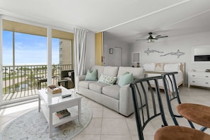 A modern living room with a sofa, coffee table, and chairs, a balcony with a view, and a ceiling fan. - Spectacular Gulf Views Close To Beach Studio 4606 (Bonita Springs)