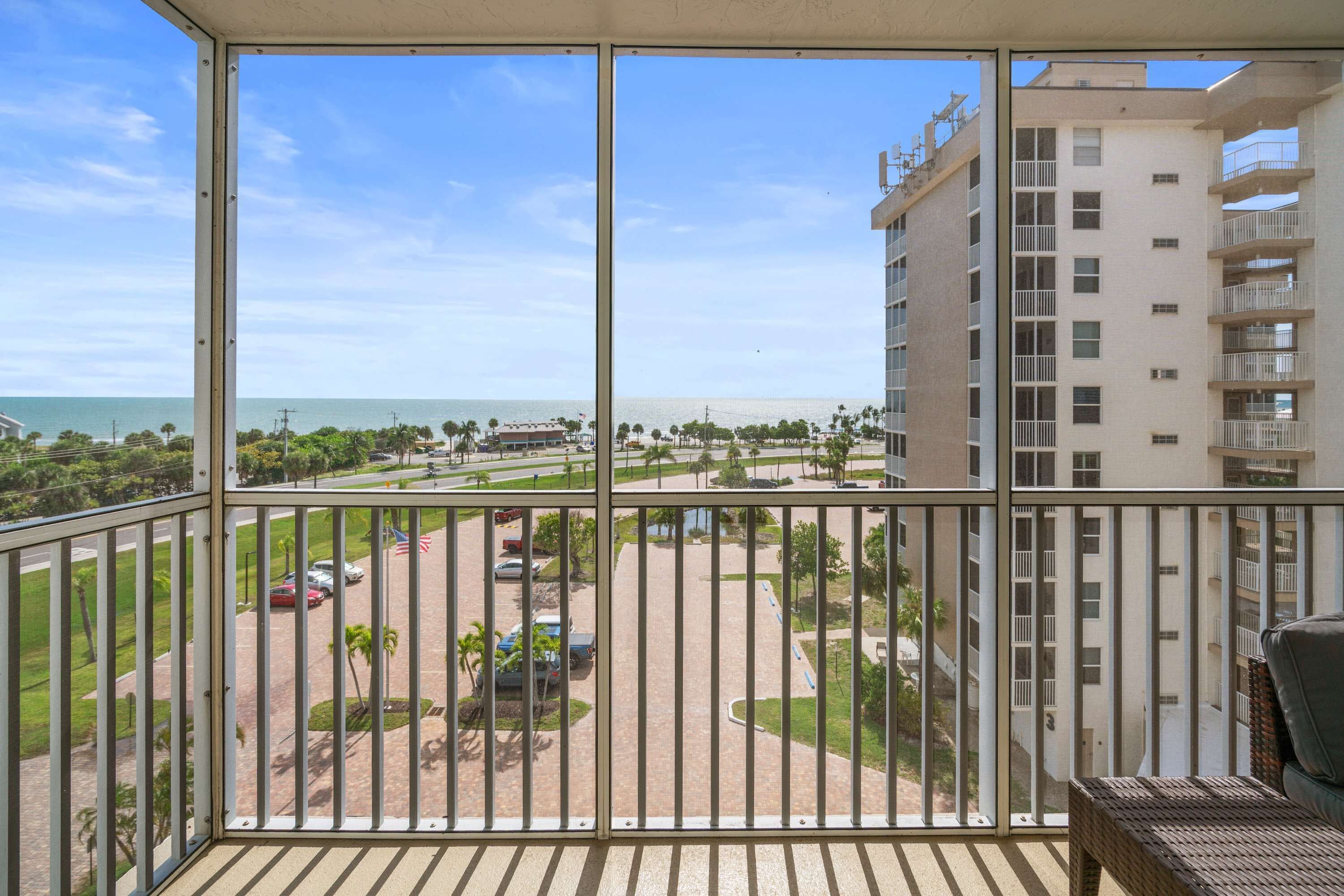 A balcony with a view of a beach, a parking area, and a multi-story building.
