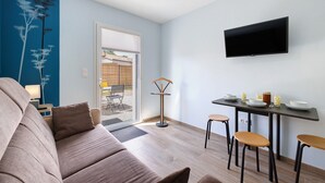 Una sala de estar moderna con un sofá, una mesa de comedor con sillas, un televisor montado en la pared y una puerta que da a un espacio exterior.