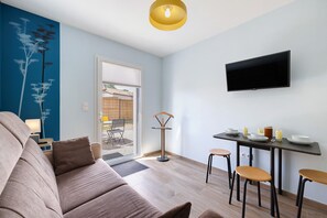 En moderne stue med sofa, spisebord med stole, fjernsyn monteret på væggen og en dør til et udendørs område.