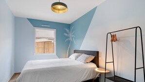 Un dormitorio con cama, ventana con persianas, estante montado en la pared y lámpara del techo.