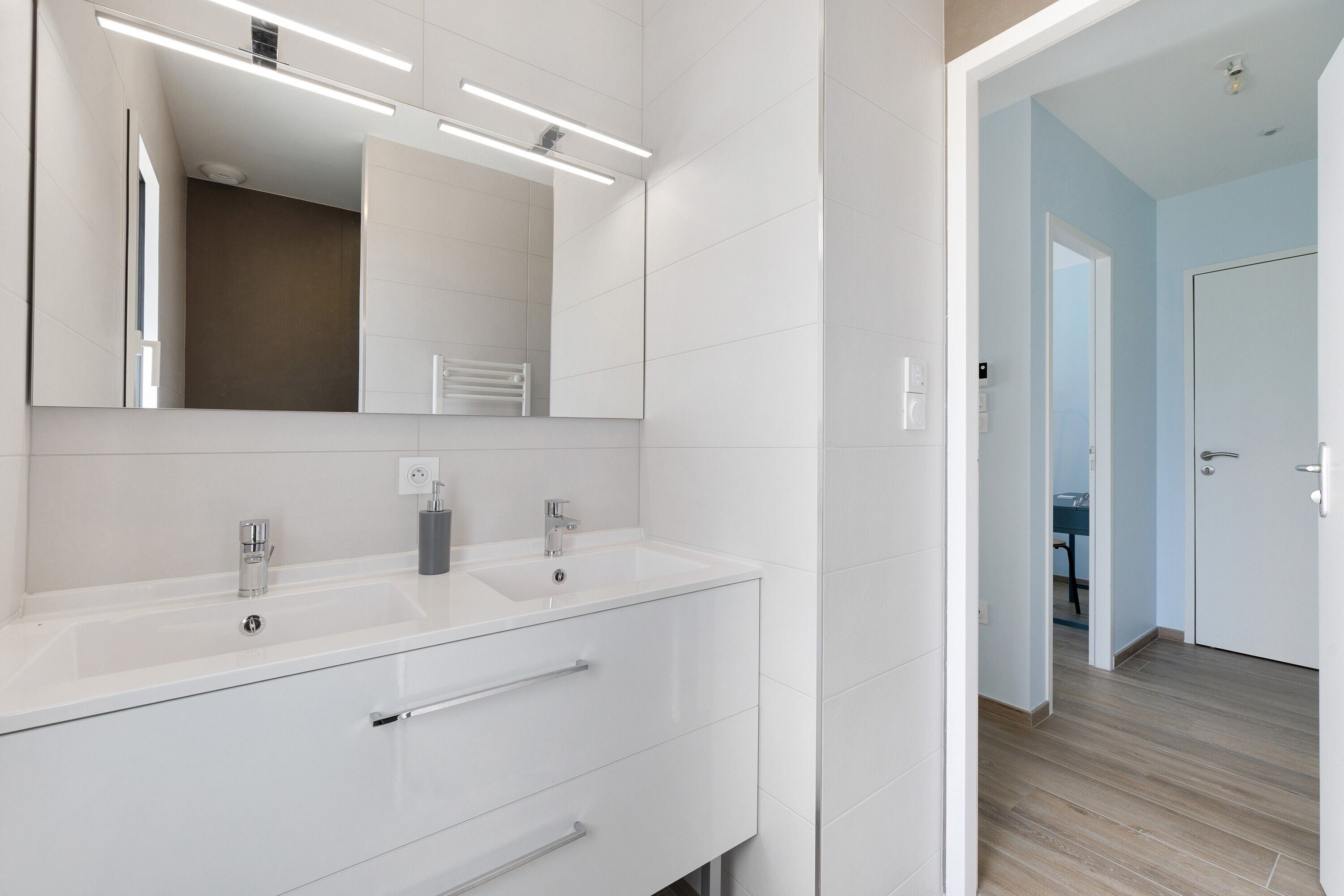 Une salle de bain moderne avec deux lavabos, un grand miroir et une douche à l’italienne.