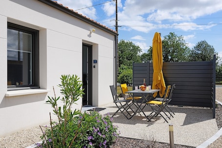 A building with a door, a window, and a patio area with a table and chairs.. Gite Logeraie – 15 Minutes from Puy du Fou