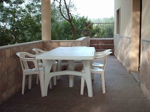 Un patio con mesa y sillas blancas, rodeado de muros de piedra y vistas al verdor.