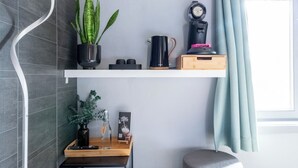 Een moderne badkamer met grijze tegels, een houten krukje, een klein tafeltje met een plant, een koffiezetapparaat en een plank met een potplant en een klok.