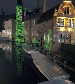 Un canal con un barco atracado, edificios con fachadas de ladrillo y follaje verde iluminado por luces.