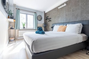 Ein modernes Schlafzimmer mit einem großen Bett, einem Heizkörper, einem Fenster mit Vorhängen, einer Wanduhr und einer Pflanze.