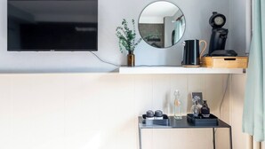 Een moderne badkamer met een flatscreen-tv, een spiegel, een koffiezetapparaat en een klein tafeltje met toiletartikelen.