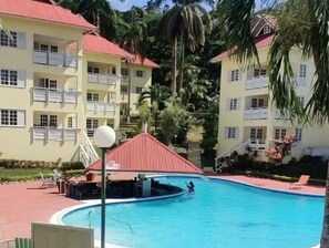 A swimming pool surrounded by a building with balconies and a red-roofed structure. - Tranquil 1BR Mystic Ridge Hideaway with Pool & AC (Ocho Rios)