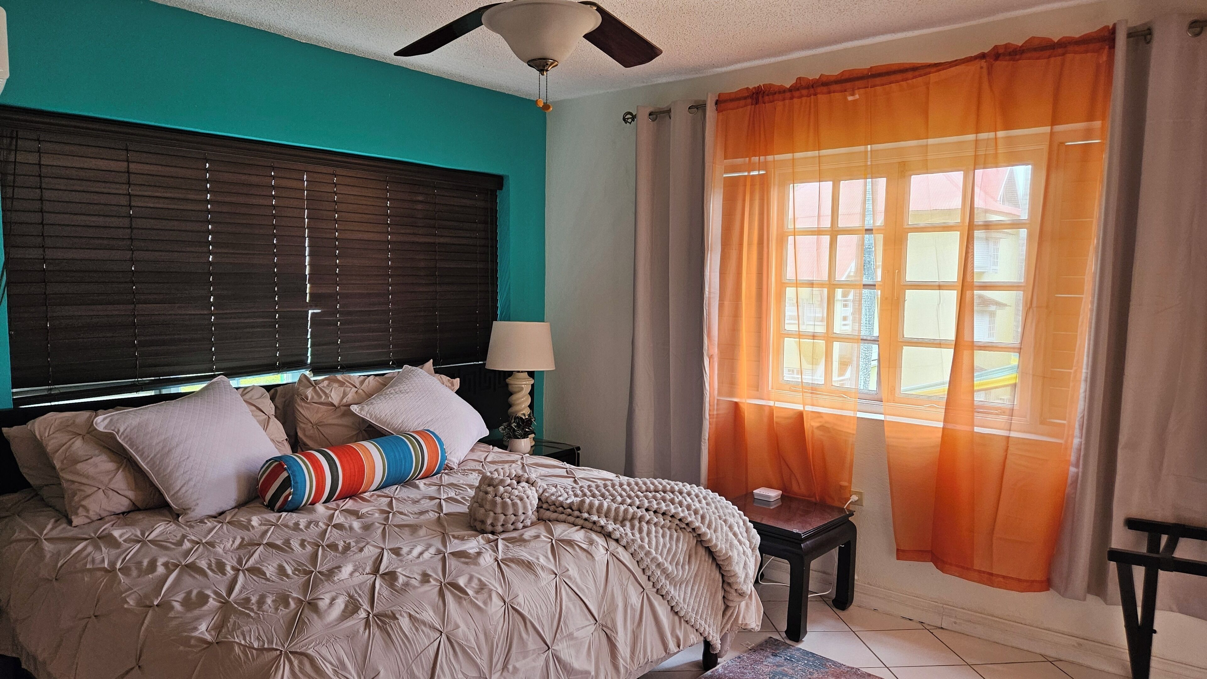 A bedroom with a bed, a ceiling fan, a window with curtains, and a nightstand with a lamp.