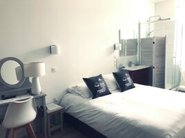 Une chambre d’hôtel comprenant un lit, un bureau avec une lampe, une chaise, un miroir, une salle de bain avec une douche et un lavabo.