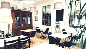 A dining area with tables and chairs, a cabinet with glass doors, and a large mirror on the wall. - Hôtel Le Galet Bleu (Fouras)