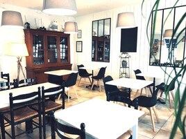 Un coin repas avec des tables et des chaises, un meuble avec des portes en verre et un grand miroir au mur.
