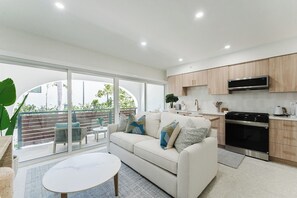 A modern kitchen with a built-in oven and microwave, a white sofa with decorative pillows, and a large sliding glass door leading to an outdoor area. - The Reserve - Boca Designer Pool Suite (Boca Raton)