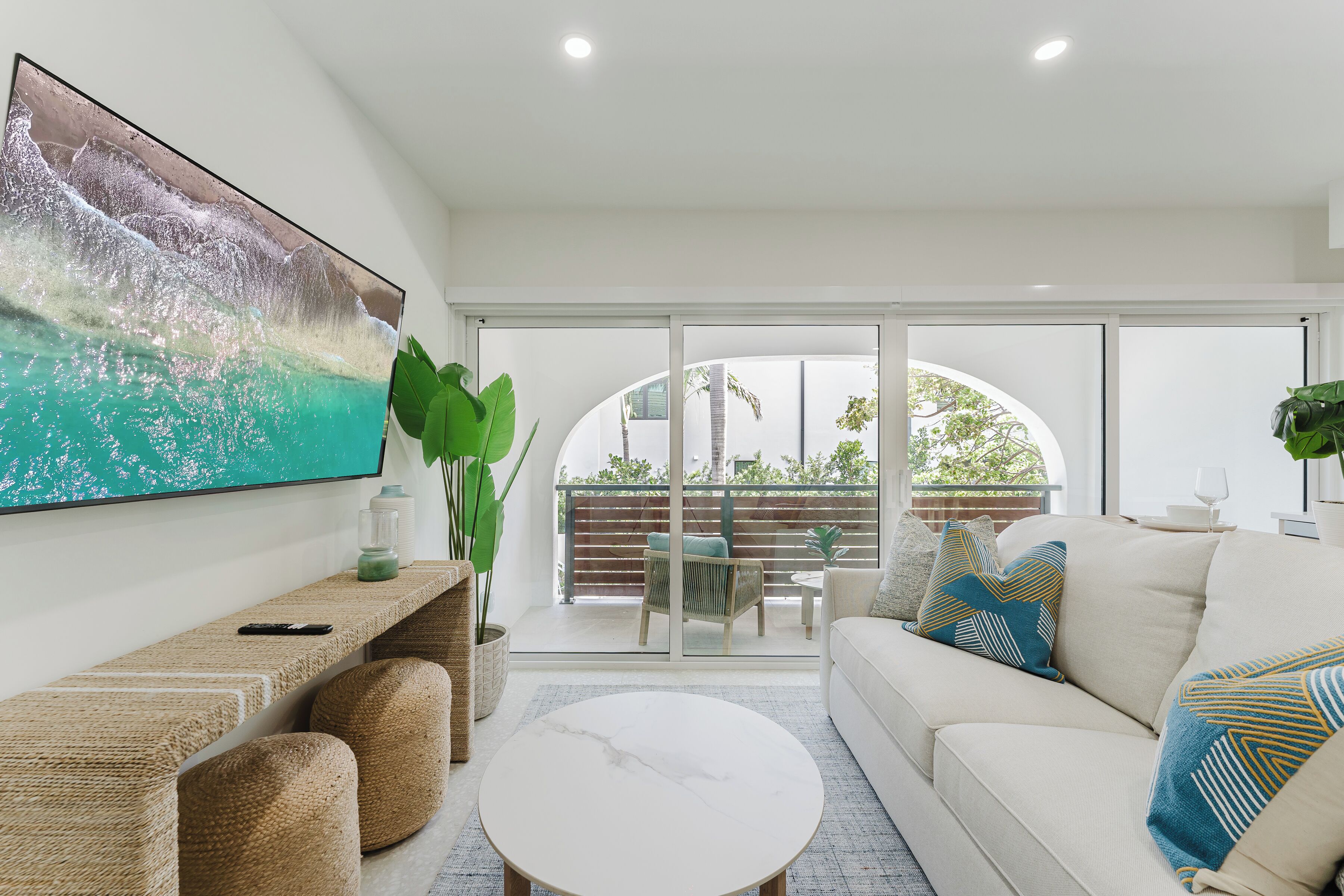 A modern living room with a large painting, a sofa, a coffee table, and a balcony with outdoor furniture.