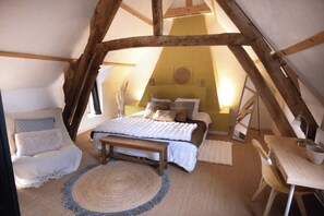 Ein gemütliches Schlafzimmer im Dachgeschoss mit einem Bett, einem Sessel, einem kleinen Tisch und einem runden Teppich.