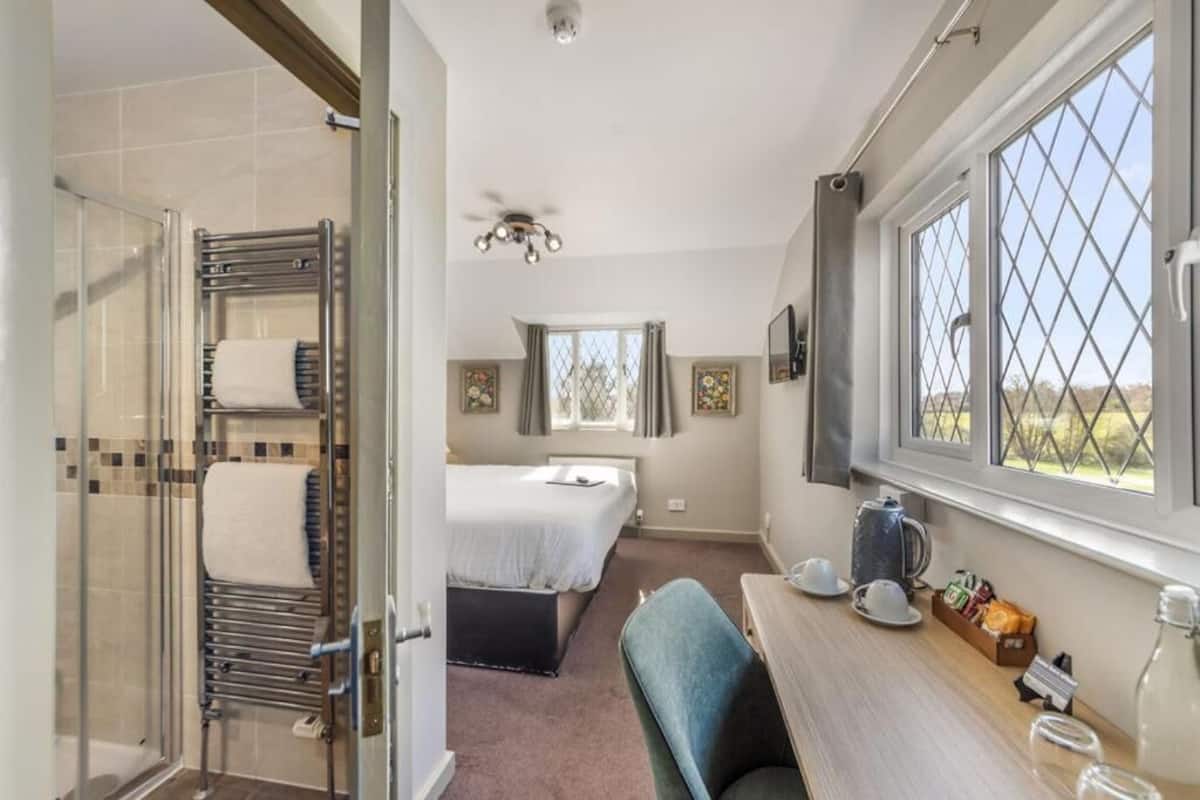 Habitación de hotel con ducha, cama, escritorio con silla y ventana con vistas.