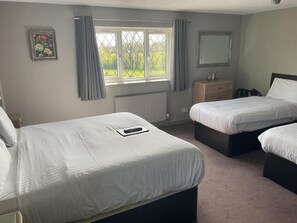 A bedroom with two beds, a window with curtains, a radiator, a dresser, and a mirror. - The Throckmorton (Alcester)