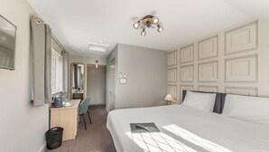 A hotel room with a large bed, a desk with a chair, a mirror, and a ceiling light fixture. - The Throckmorton (Alcester)