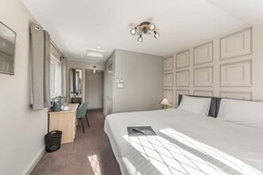 Habitación de hotel con una cama grande, un escritorio con silla, un espejo y una lámpara en el techo.