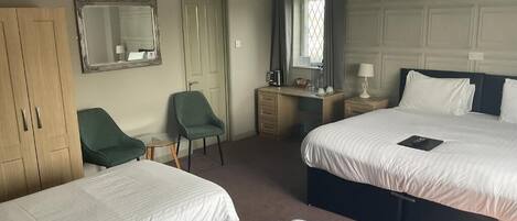 A hotel room with two beds, a desk, a chair, a wardrobe, and a mirror.
