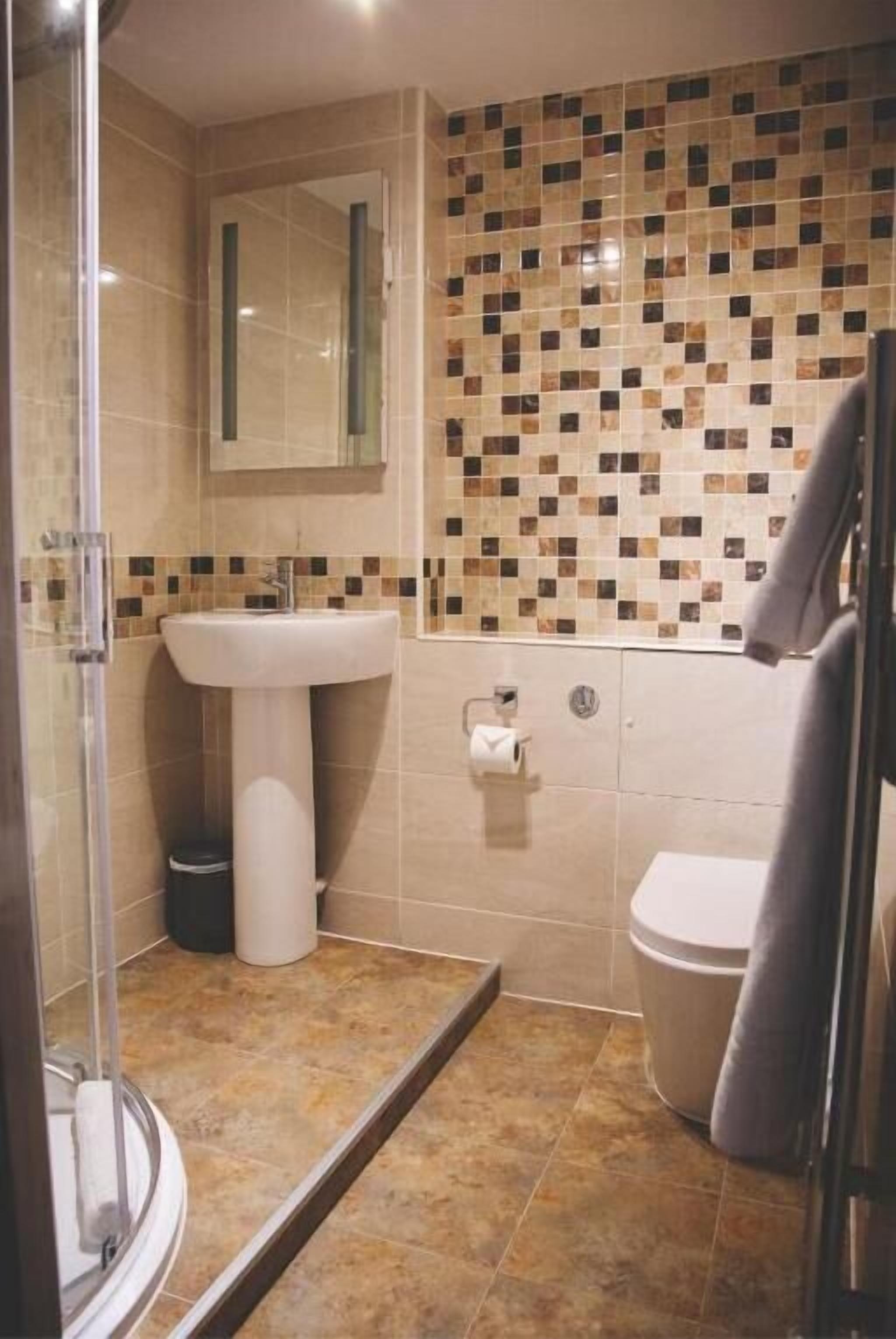 A bathroom with a shower, sink, toilet, and tiled walls.