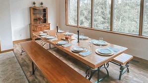 A dining room with a long wooden table set for six, a bench, and a wooden cabinet with decorative items.