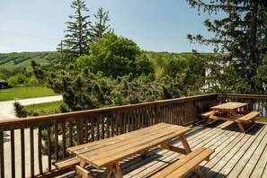 A wooden deck with picnic tables overlooking a grassy area and trees. - 6 bdrm Cottage, Private Beach Access, HotTub/Sauna (The Blue Mountains)
