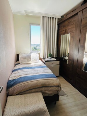 A bedroom with a bed, bedside table, dresser, and a window with curtains.