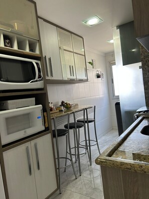 A kitchen with white cabinets, a microwave, a stove, and a small bar area with stools.