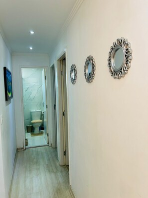A hallway leading to a bathroom with a toilet, a mirror, and a picture on the wall.