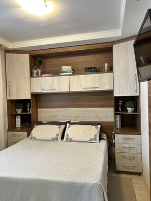 Une chambre à coucher comprenant un lit, des étagères intégrées, un téléviseur et un bureau.