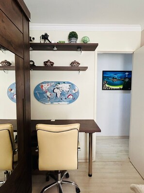 Une pièce avec un bureau en bois, deux chaises, une carte du monde, des objets décoratifs et un téléviseur fixé au mur.