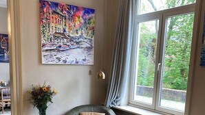 Ein Zimmer mit zwei Sesseln, einem farbenfrohen Teppich, einem Gemälde einer Brücke und einem Fenster mit Vorhängen.