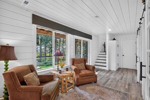 A spacious room with a large window, a staircase, and a wooden floor.