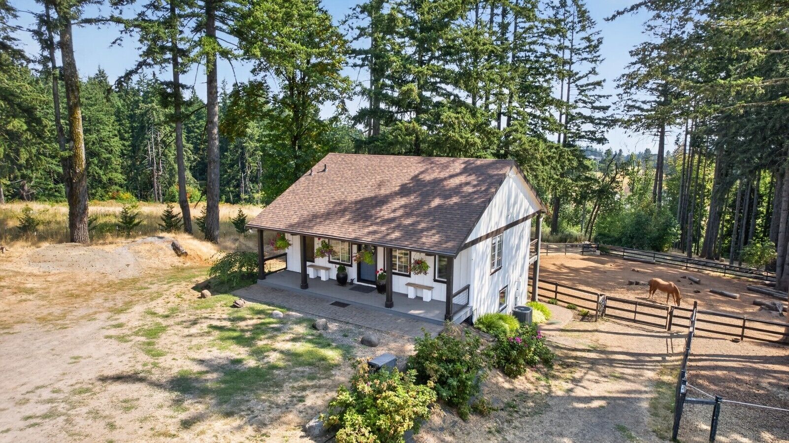 A small white building with a covered porch, surrounded by a fenced area with a horse.
