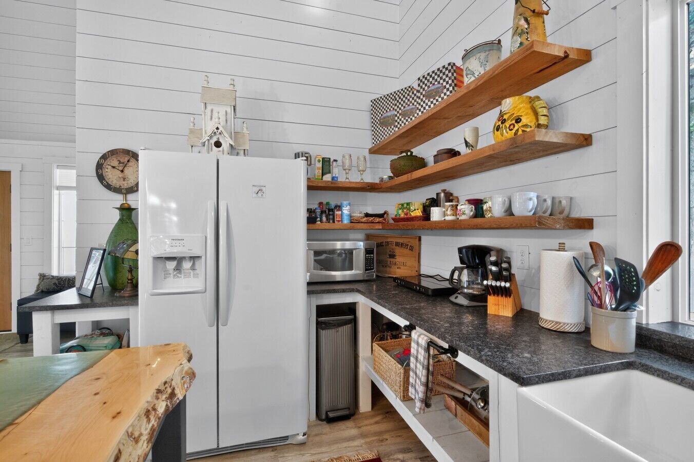 A modern kitchen with white cabinetry, a built-in oven, a microwave, and wooden shelves above the counter.