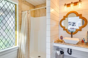 A bathroom with a shower, a sink with a mirror, and a window with a curtain.