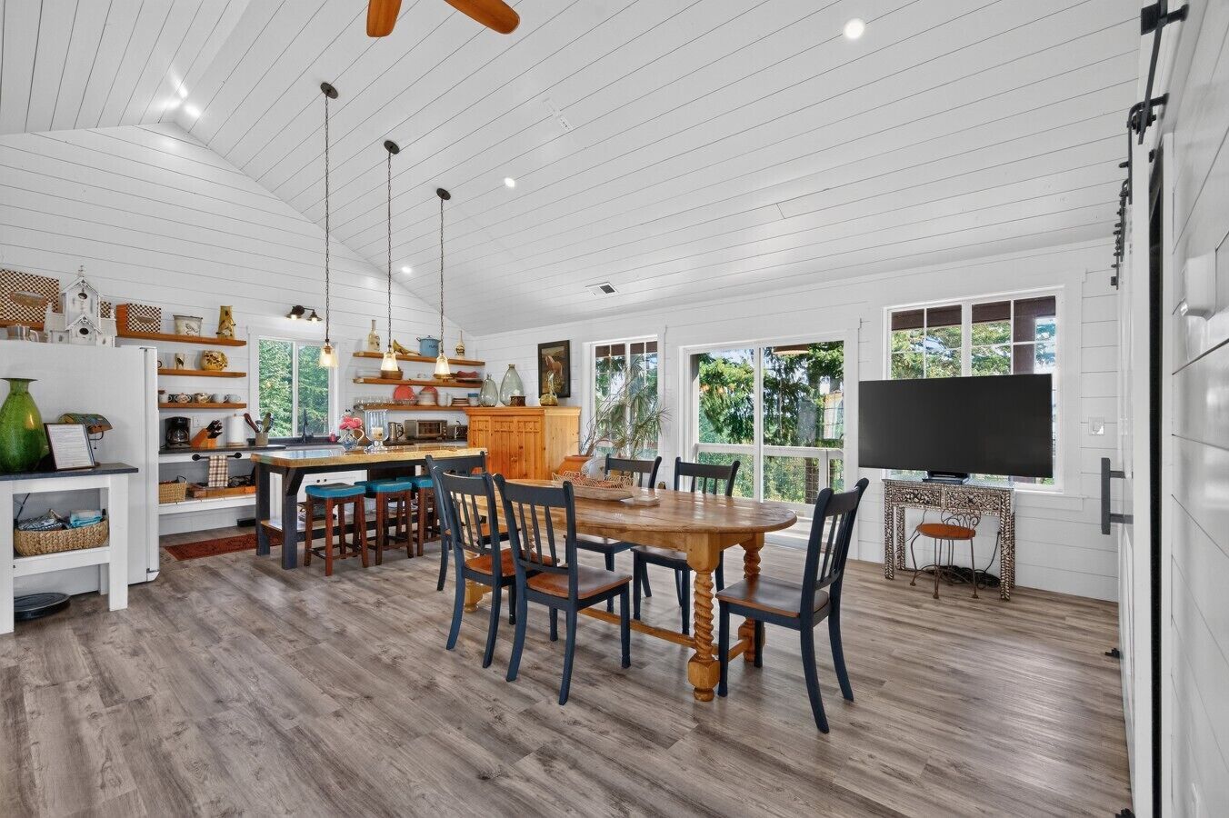 A spacious kitchen with wooden flooring, a dining area with a large wooden table and chairs, and a television on a stand.